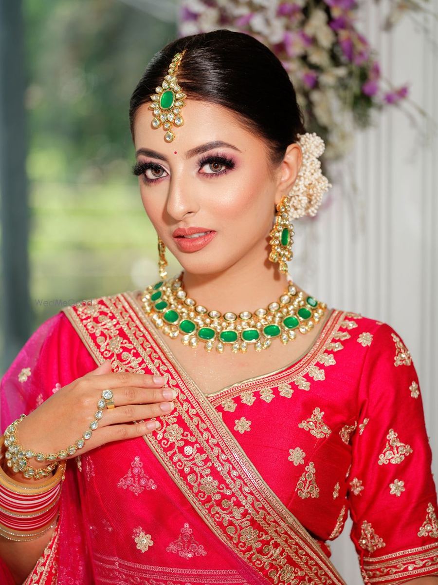 Bride in red lehenga and emerald kundan set, makeup by Illusions